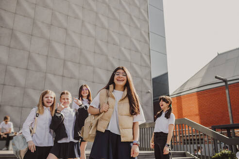 Happy girl enjoying with friends standing in front of school building - MDOF01268