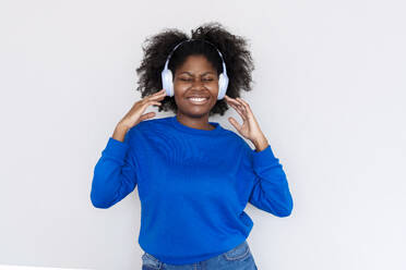 Lächelnde Afro-Frau, die Musik mit drahtlosen Kopfhörern vor weißem Hintergrund genießt - AAZF00707