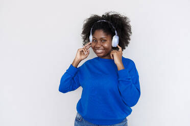 Lächelnde junge Frau genießt Musik mit drahtlosen Kopfhörern vor weißem Hintergrund - AAZF00710