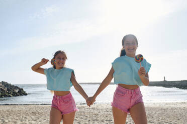Glückliche Zwillingsschwestern halten Lollipop-Bonbons am Strand - ASGF03658