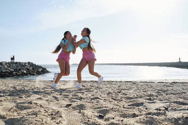 Unbekümmerte Zwillingsschwestern in Shorts spielen am Strand - ASGF03664