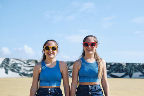 Lächelnde Zwillingsschwestern mit Sonnenbrille an einem sonnigen Tag - ASGF03666