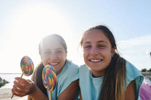 Lächelnde Zwillingsschwestern, die am Strand Lutschbonbons halten - ASGF03674