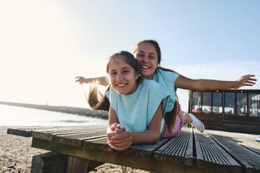 Carefree twin sisters enjoying together lying on jetty at beach - ASGF03678