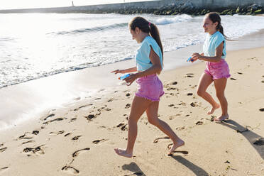 Zwillingsschwestern in Shorts spielen mit Spritzpistolen am Strand - ASGF03686