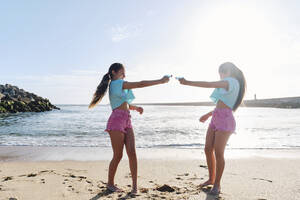 Zwillingsschwestern spielen mit Spritzpistolen am Strand an einem sonnigen Tag - ASGF03691