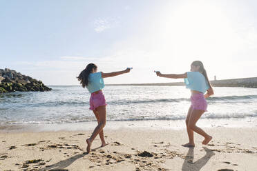 Glückliche Zwillingsschwestern spielen Wasserschlacht mit Spritzpistolen am Strand - ASGF03692
