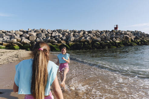 Zwillingsschwestern in passenden Outfits haben Spaß am Strand am sonnigen Tag - ASGF03695