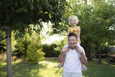 Happy father carrying daughter on shoulders in garden - SVKF01415