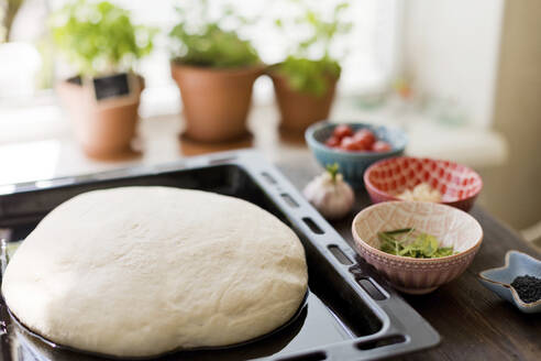 Focaccia bread dough kept in tray with ingredients at table - ONAF00546