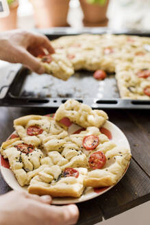 Hands of man with freshly baked focaccia bread at table - ONAF00549