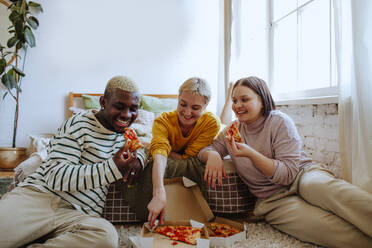 Junge Freunde, die zu Hause auf dem Bett sitzend Pizza genießen - MDOF01297