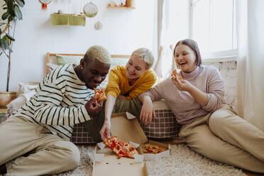 Glückliche junge Freunde, die zu Hause auf dem Bett sitzend eine Pizza genießen - MDOF01298