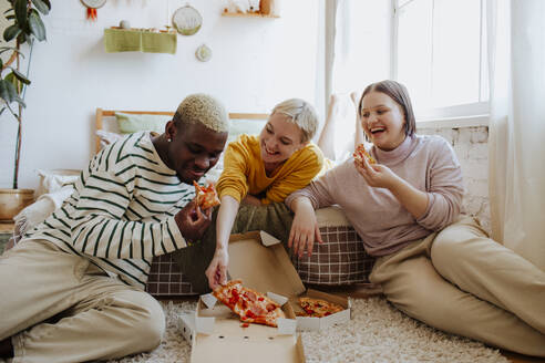 Happy young friends enjoying pizza sitting on bed at home - MDOF01298