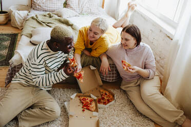 Young friends enjoying pizza sitting on bed at home - MDOF01299