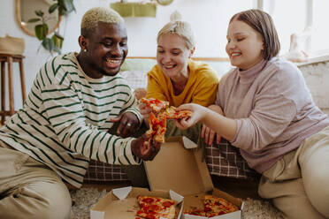 Glückliche junge Freunde, die auf dem Bett sitzend Pizza genießen - MDOF01300