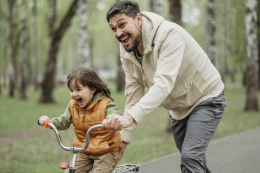 Glücklicher Vater hilft seinem Sohn beim Fahrradfahren im Park - ANAF01524