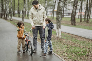 Glücklicher Vater und Söhne stehen mit Fahrrad im Park - ANAF01527