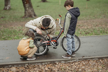 Vater repariert Fahrrad mit Sohn im Park - ANAF01530