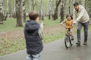 Vater unterstützt Sohn beim Fahrradfahren im Park - ANAF01531