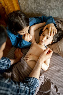 Vater prüft die Temperatur eines kranken Kindes mit einem Thermometer zu Hause - ANAF01538