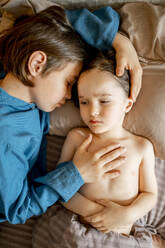 Junge kümmert sich um seinen kranken Bruder, der zu Hause im Bett liegt - ANAF01543