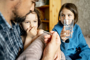 Junge, der seinem kranken Sohn zu Hause ein Glas Wasser gibt, und Vater, der ihm Medikamente gibt - ANAF01547