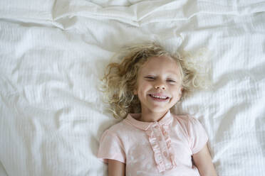 Lächelndes Mädchen entspannt sich auf dem Bett zu Hause - SVKF01426