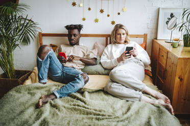 Young couple using smart phones resting on bed at home - MDOF01315