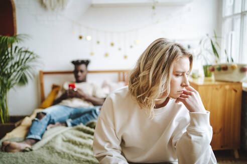 Sad woman on bed with boyfriend using phone in background - MDOF01320