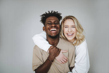 Junges Paar mit Arm um lachend gegen grauen Hintergrund - MDOF01324