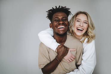 Happy young couple with arm around laughing against gray background - MDOF01325