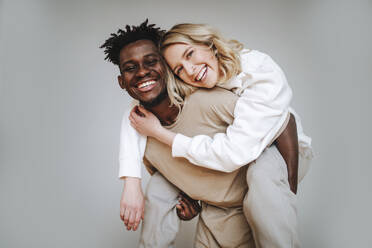 Cheerful young man piggybacking girlfriend against gray background - MDOF01327