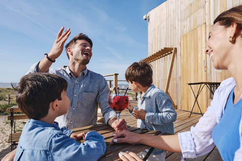 Happy mother and father sitting at table with children enjoying vacations on sunny day - ASGF03728