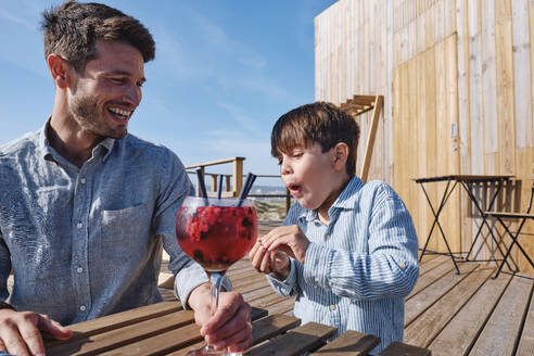 Boy with happy father holding glass of juice at table - ASGF03729