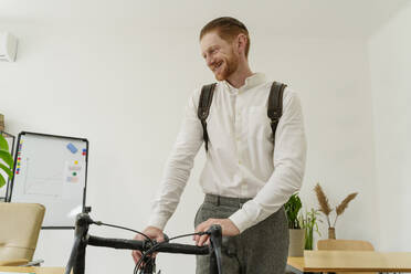 Glücklicher Geschäftsmann mit Fahrrad im Büro stehend - OSF01628