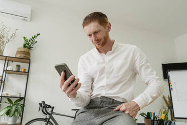 Lächelnder Geschäftsmann, der ein Smartphone im Büro benutzt - OSF01649