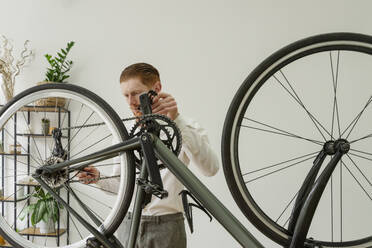 Businessman repairing bicycle in front of wall - OSF01653