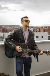 Junger Musiker mit Gitarre auf dem Dach stehend - JCCMF10472