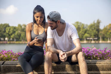 Man looking at smart phone held by woman sitting on bench - IKF00846