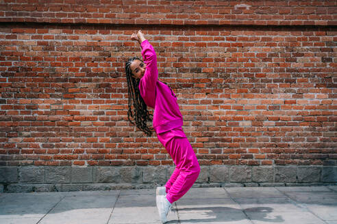 Happy young woman dancing in front of brick wall - GDBF00064