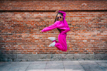 Cheerful woman jumping in front of brick wall - GDBF00068
