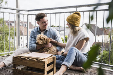 Glückliches Paar hat Spaß mit Hund auf Balkon - UUF28781