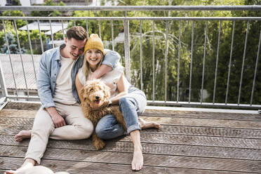 Liebendes junges Paar mit Hund auf dem Balkon sitzend - UUF28786