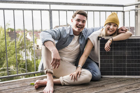Glückliches Paar sitzt mit Sonnenkollektor auf dem Balkon - UUF28794