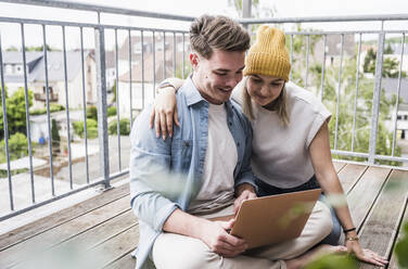 Happy couple using laptop on balcony - UUF28811