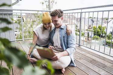 Happy man and woman using laptop on balcony - UUF28812