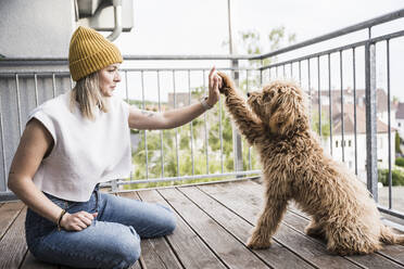 Lächelnde Frau mit Hund, die sich auf dem Balkon gegenseitig abklatschen - UUF28823