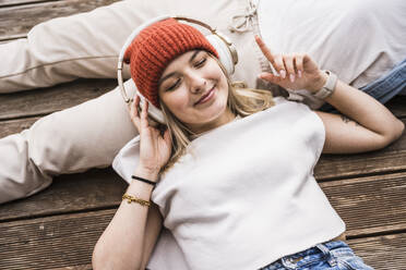 Lächelnde junge Frau mit drahtlosen Kopfhörern, die gestikuliert und Musik hört - UUF28825