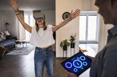 Happy woman wearing virtual reality simulator with man holding tablet PC - UUF28829